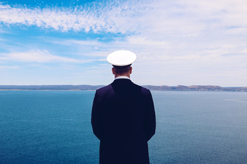 Strong posture of a captain looking at the sea and faraway land on the horizon. Navy/Cruise ship concept. Outdoor shot. - obrazy, fototapety, plakaty