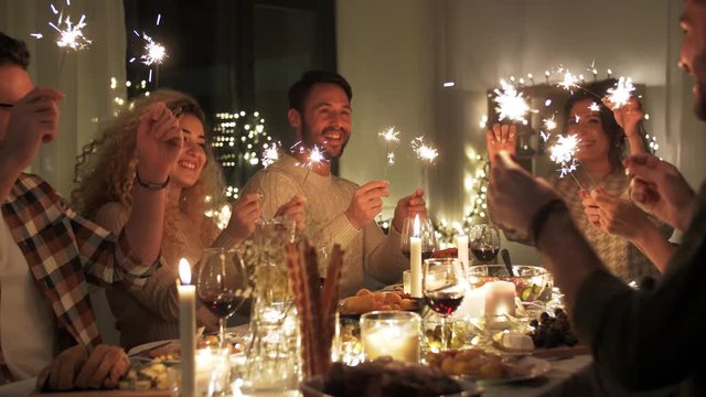 holidays, celebration and people concept - happy friends with sparklers having christmas dinner at home