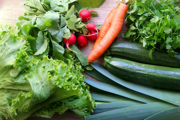 Various vegetables and herbs on a table: leek, lettuce, asparagus, parsley, carrot and radish. Top view.