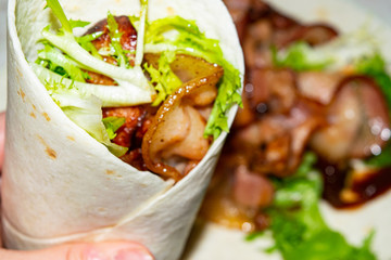 Leafy salad, sliced vegetables, sauce and fried bacon slices wrapped in pita bread. Delicious homemade Shawarma. Close up.