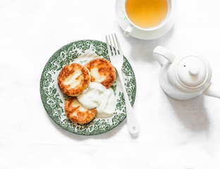 Breakfast served table - cottage cheese pancakes with sour cream, green tea on a light background, top view