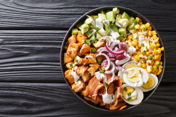 Healthy salad of fried chicken, avocado, corn, onion, eggs seasoned with yogurt close-up in a plate. horizontal top view