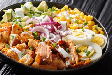Tasty fresh salad of chicken, avocado, corn, onion, eggs with spicy dressing closeup in a plate. horizontal
