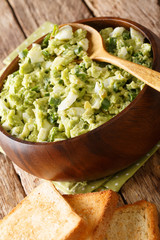 Tasty light avocado salad with eggs and green onions close-up in a bowl served with toasts. vertical