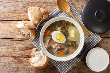 portion of green borsch from sorrel, vegetables, eggs with meat in a saucepan served with bread and sour cream closeup. horizontal top view