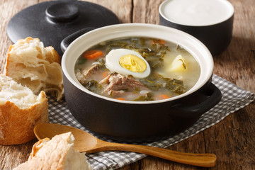 portion of green borsch from sorrel, vegetables, eggs with meat in a saucepan served with bread and sour cream closeup. horizontal