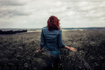 young red haired woman walking away in a wheat field