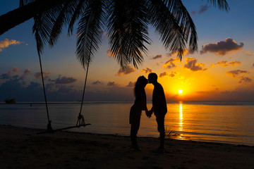 Silhouetted couple in love kisses on the beach during sunset.