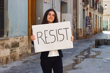 attractive  young woman activist hold up protesting sign saying "Resist" in the city, dark air. Place for your text in copy space.