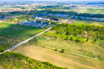 Aerial view of residential houses neighborhood and apartment building complex at sunset. Tightly packed homes, driveway surrounds green tree flyove. Suburban housing development