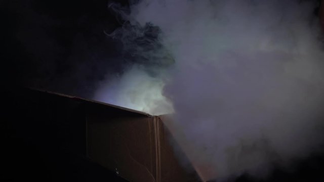 A man opens a cardboard box from which smoke comes and a multi-colored light shines. The concept of magic and magic, surprise