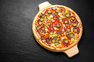 Mexican pizza on a black background, tomato-based with mozzarella, salami, beef, hot and sweet peppers, corn, and lightly salted cucumber