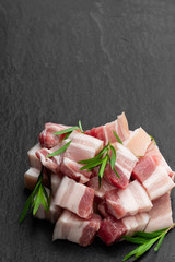 Belly pork slices with tarragon herb on black stone background