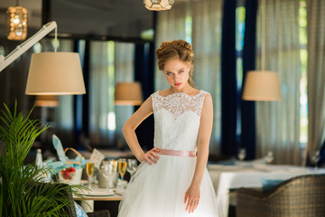 Naklejka premium Portrait of pretty young blond bride with hairdressing and white dress posing at restaurant