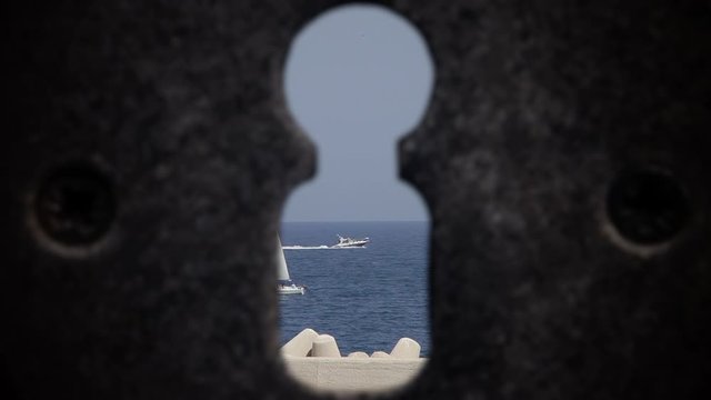 Seen through a keyhole while in quarantine at home: many sailboats at sea, near a pier, in a calm day, preparing for a regatta.
