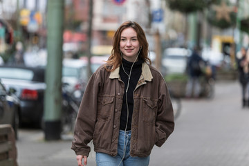 Young Caucasian Woman Smiling on Sidewalk Listening to Earphones