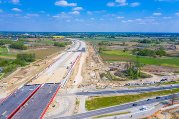 Aerial panorama top down view of an unfinished asphalt covered road with dirt, tracks of heavy machinery at construction site. The road to nowhere.