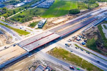 Aerial panorama top down view of an unfinished asphalt covered road with dirt, tracks of heavy machinery at construction site. The road to nowhere.