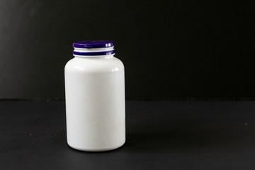 a white plastic jar full of pills on a dark background