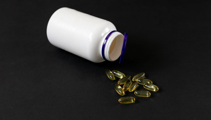 an overturned white plastic jar with scattered pills omega-3