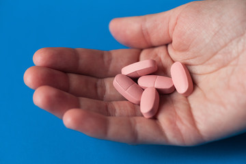 Fototapeta na wymiar Hand of woman holding pink pills. Vitamins in woman's hand. Isolated on blue background.