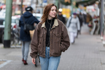 Young Woman in Jeans Walking on Sidewalk Listening to Earphones