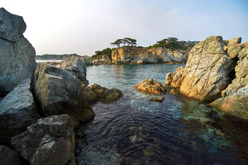 Fototapeta na wymiar Rocky high island in the ocean. Rocky high island in Orlik Bay in the Sea of Japan. In the foreground are stones and clear water. Far East.