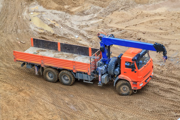 Obraz premium top view of a flatbed truck with a blue crane arm parked on a sand construction site