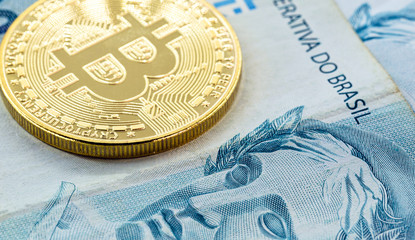 electronic bitcoin coins, with a hundred dollar bill in the background. Devaluation of the Brazilian real against the decentralized currency.