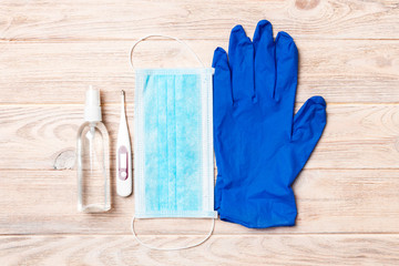 Top view of alcohol hand sanitizer, latex gloves, digital thermometer and surgical mask on wooden...
