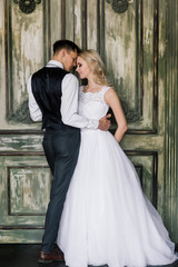 Fototapeta premium Cute wedding couple in the interior of a classic studio decorated. They kiss and hug each other.