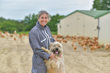 Portrait of a farmer petting her dog and standing in the middle of her chicken farm