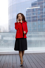 Obraz premium A beautiful business woman in red suit, has a conversation on a her smartphone, a business meeting online.