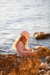 Happy pretty girl walks along the sea coast against the background of the sea, from behind a beautiful landscape. The child draws in a notebook