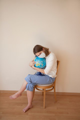 little girl in medical mask sitting on a chair with a global