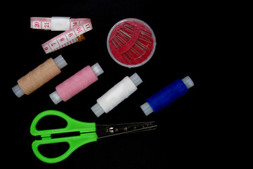 A sewing kit, several spools, a needle and scissors lie on a black background.