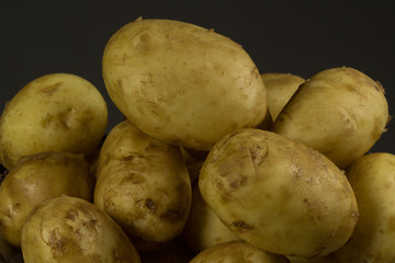 Raw fresh organic potatoes on black wooden table against dark background.