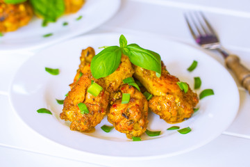 fried chicken pieces in a white plate and a sprig of Basil on the table close-up. lunch in the form of fried chicken and greens. background with cooked chicken pieces, basil sprigs .