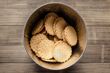 Closeup and top view of integral biscuits on a metal round box on a wooden table.