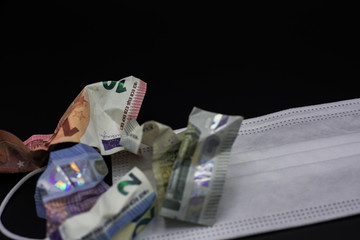 Detail of wrinkled euro banknotes and white prevention mask on a black background. Concept of crisis in the euro area with copy space.