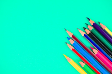 Many different color wood pencil crayons placed on top of a light blue background