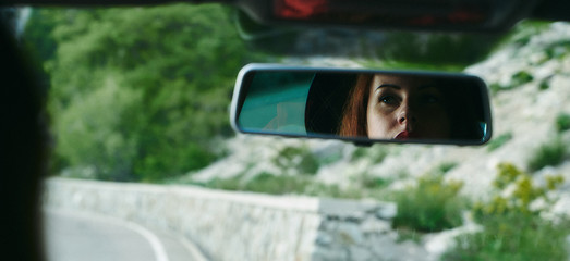 A young girl in a car looks at herself in the mirror, beautiful pensive eyes.