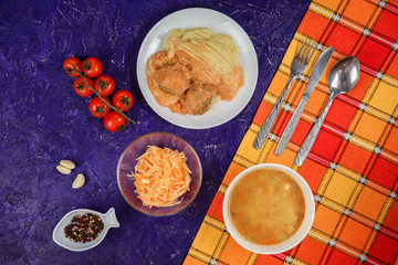 Delicious lunch set contains soup, potatoes and meat balls, carrot salad. Served on the violet texture table coverd with orange towel. 
