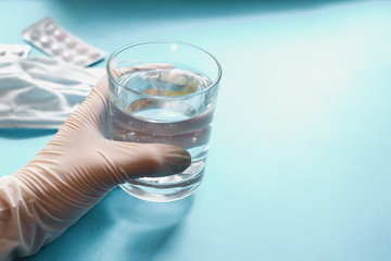 Coronavirus prophylaxis with surgical masks and gloves. Medical mask, pills, drugs, water in a glass. Light blue background. Free space for text. Hands in gloves.