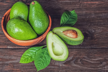 whole avocados in a wooden bowl and half-ripe avocado on a wooden table close-up. background with ripe avocado close-up. avocado and leaves.