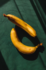 Bananas on a green background. Summer abstract creative photography with sun light and shadows.