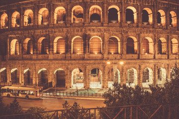 Fototapeta premium night Coliseum with windows lit from the inside and a passing bus