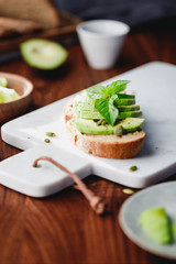 Avocado toast with pepitas and fresh basil on a white marble cutting board. Home cooking, healthy eating concept.