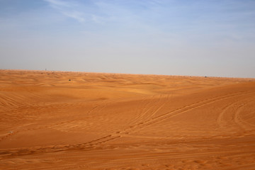 Fototapeta na wymiar Red sand dunes in Sharjah, UEA during a sunny day. A lot of sand and plenty of tire marks and some footprints since there has been tourists doing dune bashing, walking and enjoying the Middle East.