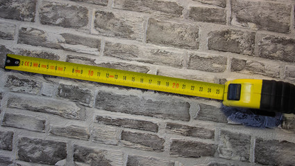 Yellow construction tape measure on a brick background.
